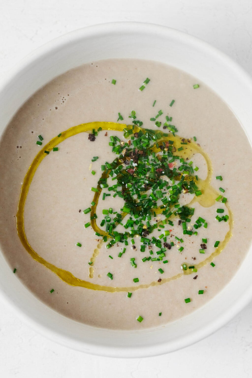 A top-down view of a large bowl of creamy, light brown mushroom soup garnished with chives.